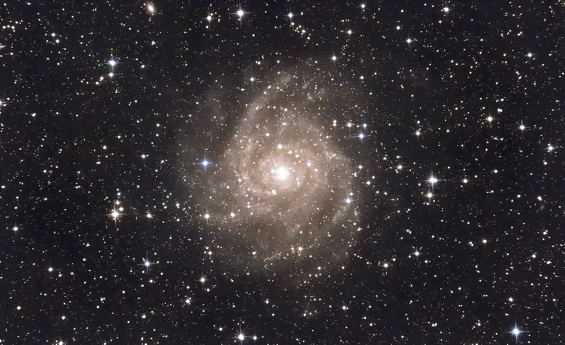 Galaxie IC 342 photographiée au télescope : spirale vue de face aux bras largement ouverts et bleutés, noyau jaune, dans un champ d'étoiles très dense de la constellation de la Girafe.