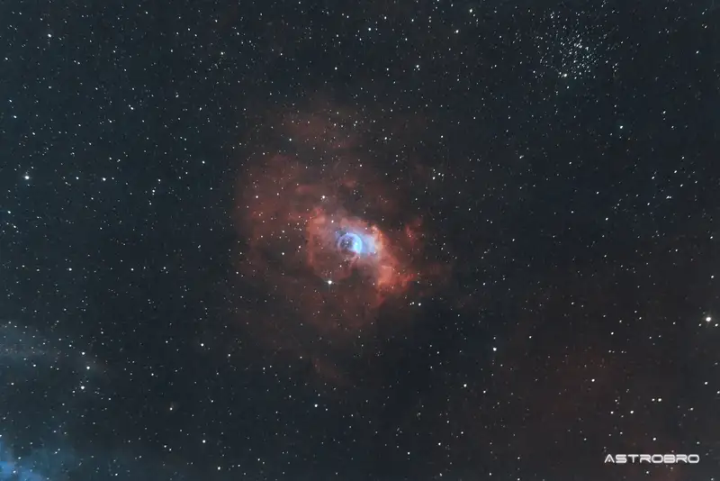 Nébuleuse de la Bulle (NGC 7635) photographiée au télescope : sphère de gaz presque parfaite se détachant sur un fond d'hydrogène rouge, avec l'étoile responsable décalée du centre, dans Cassiopée.