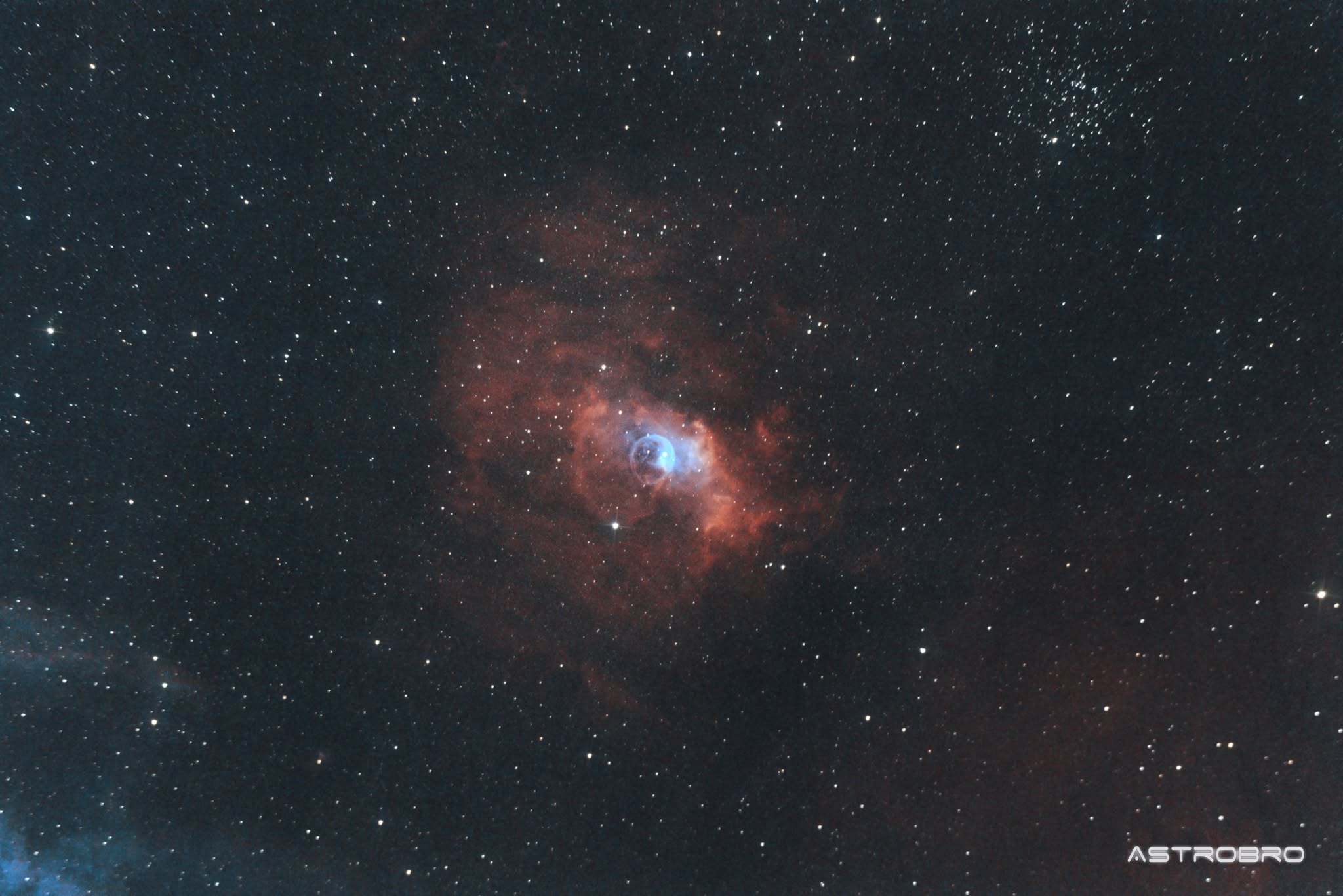 Nébuleuse de la Bulle (NGC 7635) photographiée au télescope : sphère de gaz presque parfaite se détachant sur un fond d'hydrogène rouge, avec l'étoile responsable décalée du centre, dans Cassiopée.