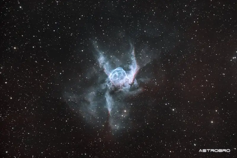 Nébuleuse du Casque de Thor (NGC 2359) photographiée au télescope : bulle bleu-vert flanquée de deux extensions latérales évoquant des ailes de casque, sur fond d'hydrogène rouge, dans le Grand Chien.