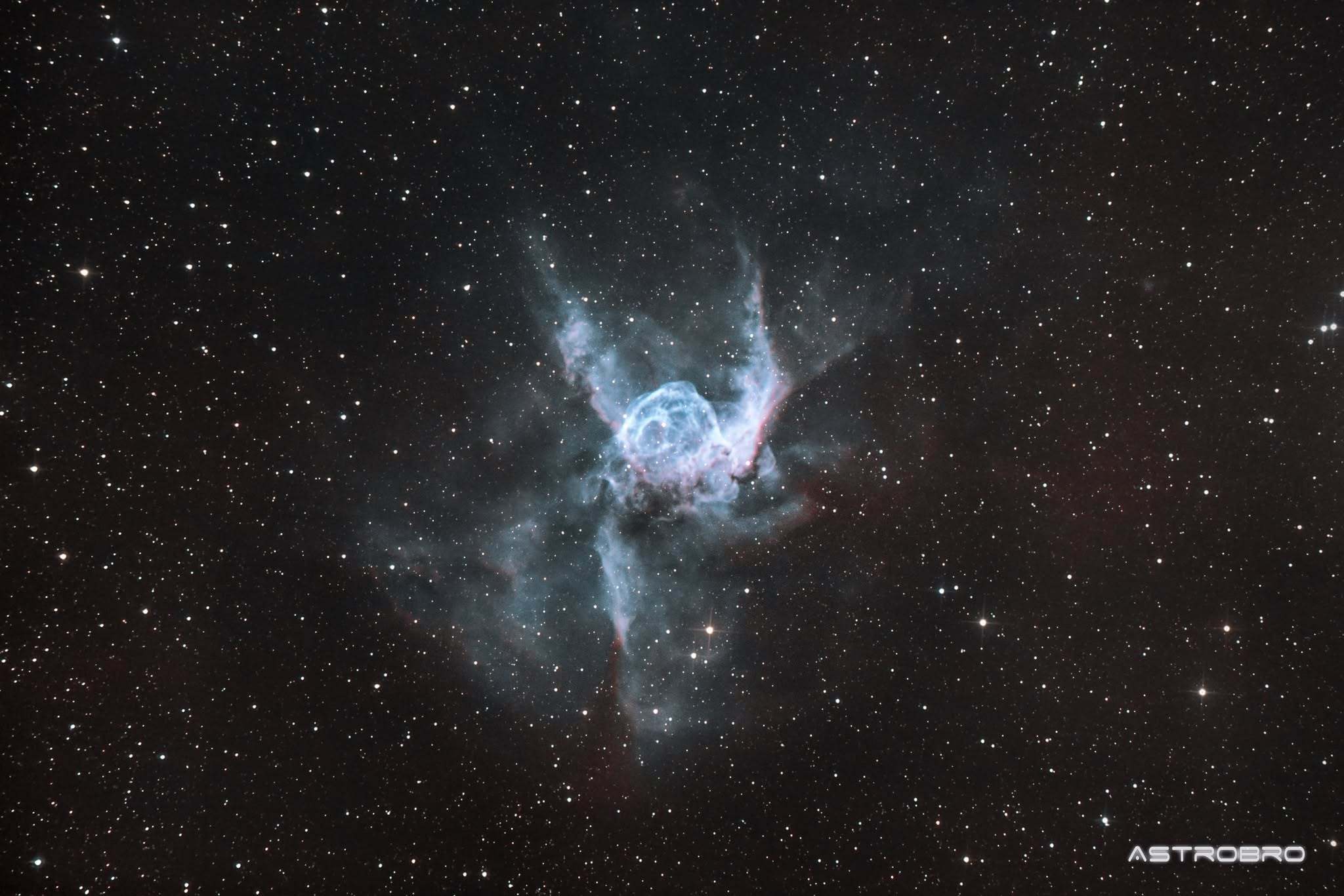 Nébuleuse du Casque de Thor (NGC 2359) photographiée au télescope : bulle bleu-vert flanquée de deux extensions latérales évoquant des ailes de casque, sur fond d'hydrogène rouge, dans le Grand Chien.