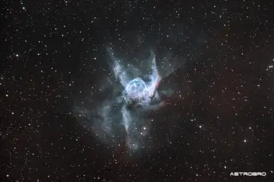 Nébuleuse du Casque de Thor (NGC 2359) photographiée au télescope : bulle bleu-vert flanquée de deux extensions latérales évoquant des ailes de casque, sur fond d'hydrogène rouge, dans le Grand Chien.