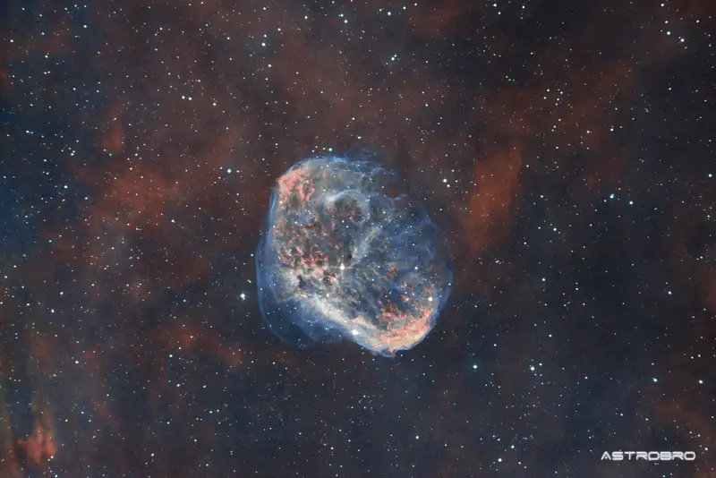 Nébuleuse du Croissant (NGC 6888) photographiée au télescope : coquille de gaz en forme de croissant, filaments rouges et cœur bleu-vert, entourée d'un halo d'hydrogène, dans le Cygne.